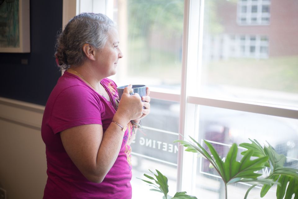 A woman holding a mug of coffee by a sunny window
