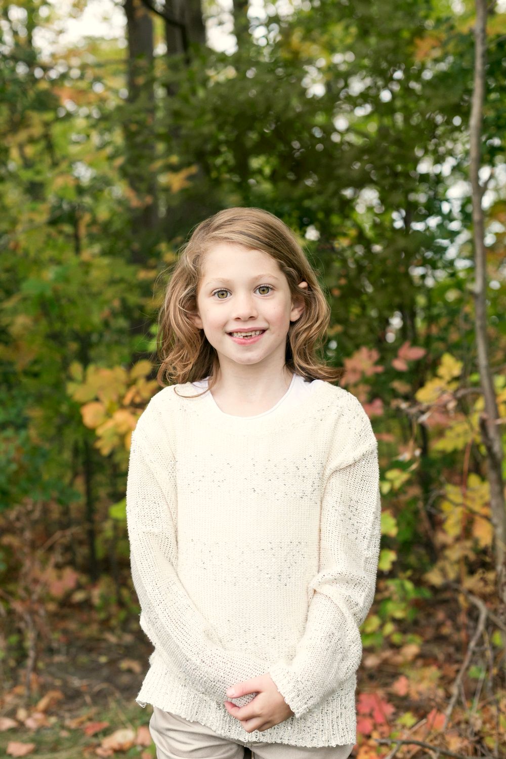 A young girl in a white sweater smiling among autumn trees