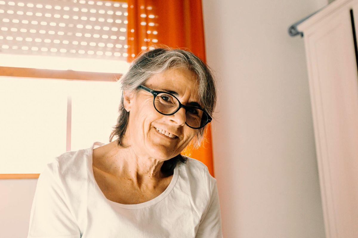 An older woman with glasses smiling in warm window light