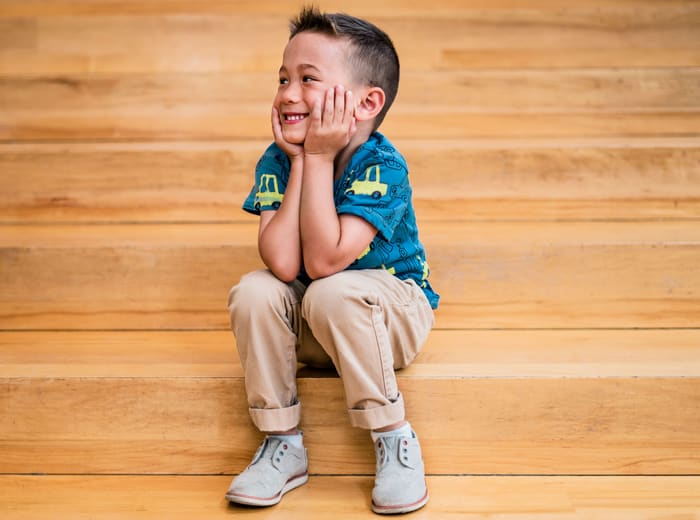 A boy sitting on wooden steps, chin in his hands, grinning