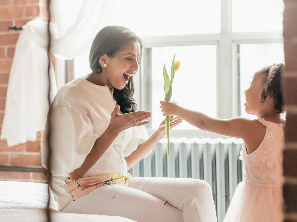 A girl handing her mother a bunch of flowers by a sunny window