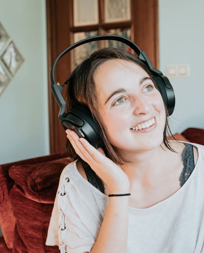 A woman on her sofa, smiling, listening to headphones