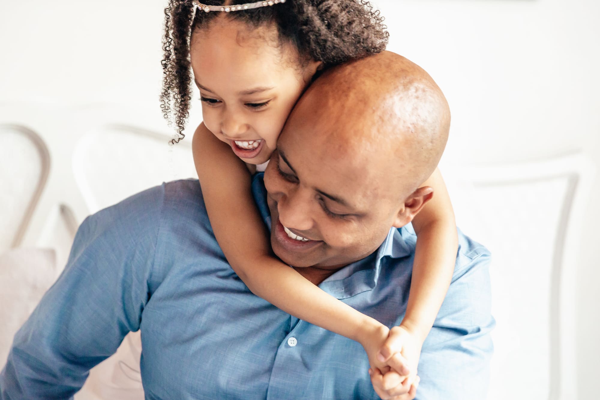 A father laughing as his young daughter hugs him from behind