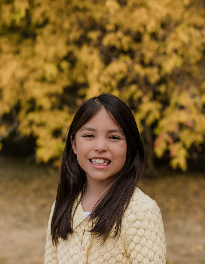 A smiling girl in a yellow sweater outdoors in autumn