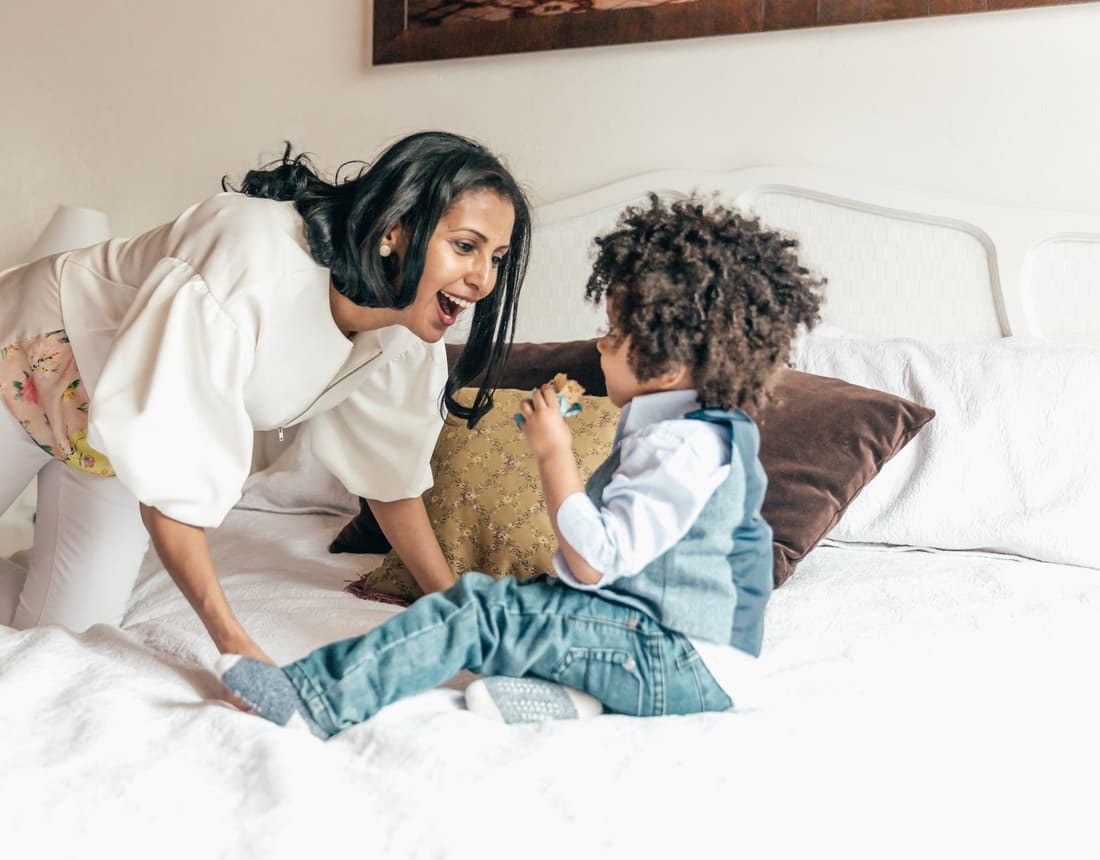 A mother and her young son laughing together on a bed
