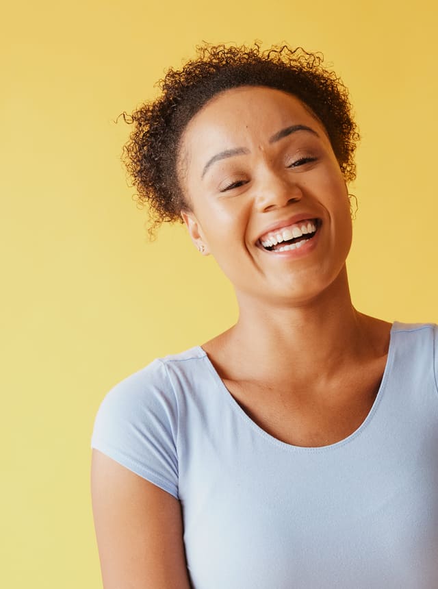 A woman laughing against a yellow wall