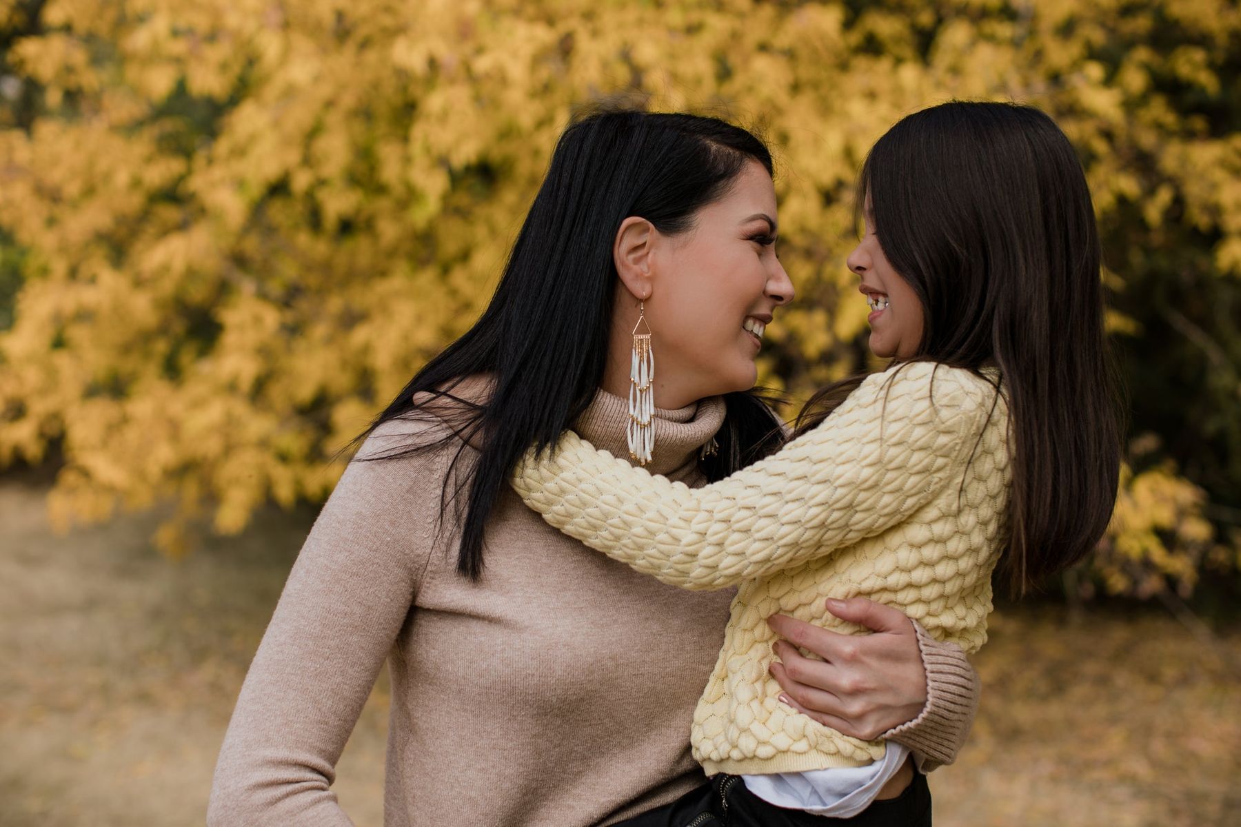 A mother hugging her young daughter outdoors in autumn