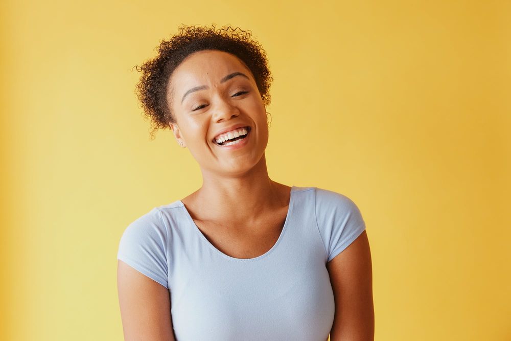A woman laughing against a yellow wall