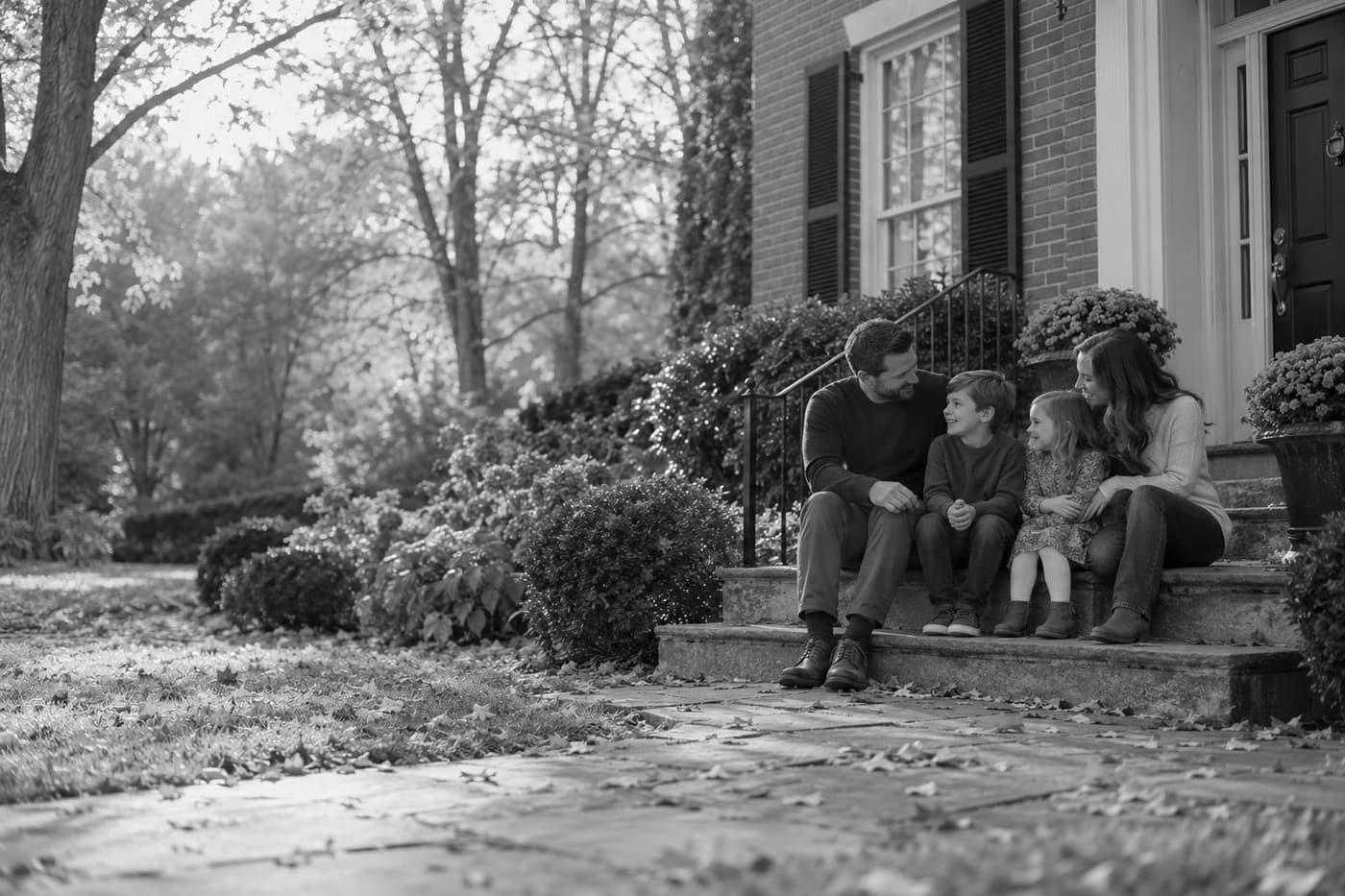A family of four sitting together on the brick front steps of a house in autumn.