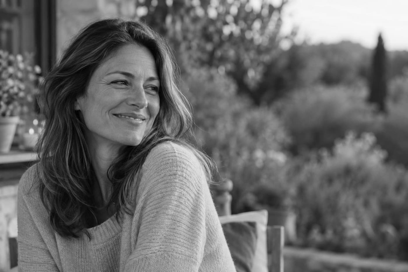 A woman in a sweater laughing outdoors in evening light.