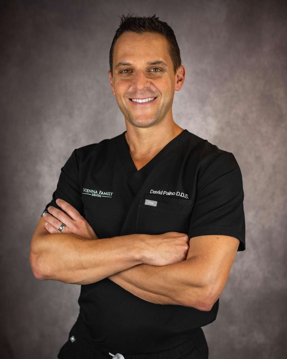 Dr. David Paino, DDS, in black scrubs, arms crossed, smiling
