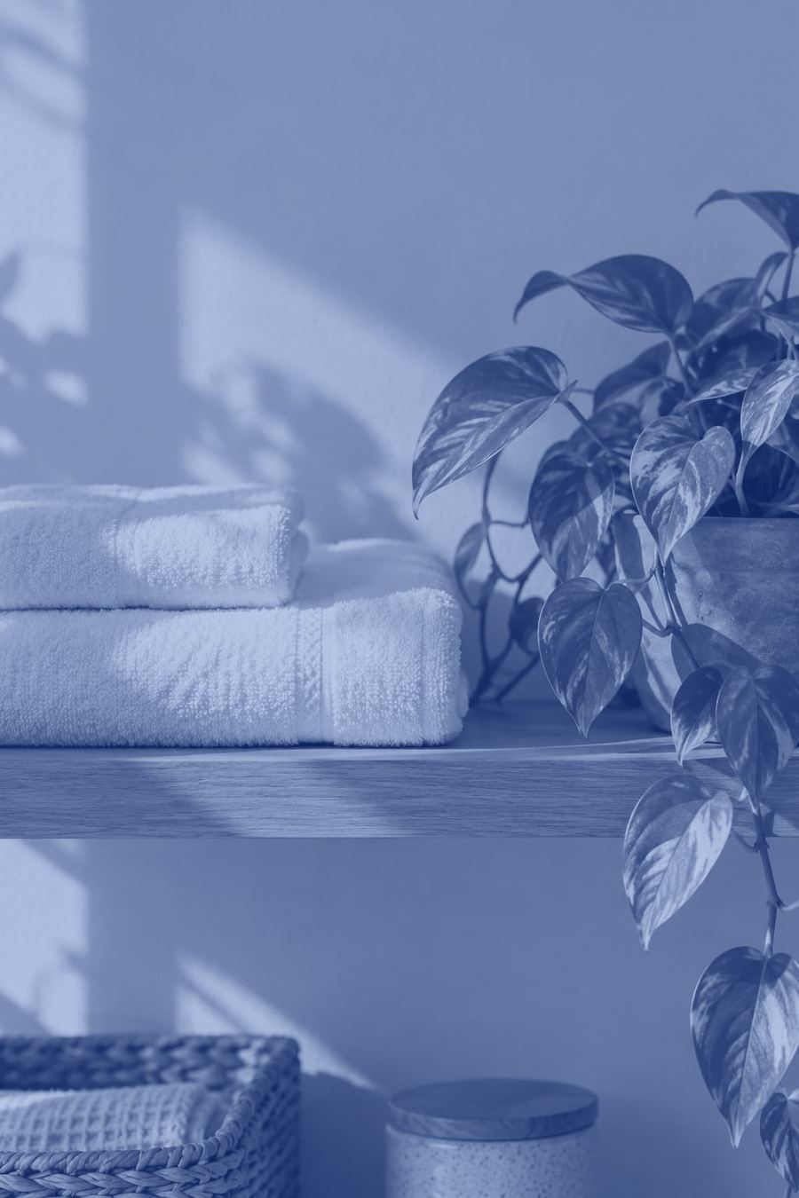 Soft folded towels and a trailing plant on a wooden shelf, in evening blue