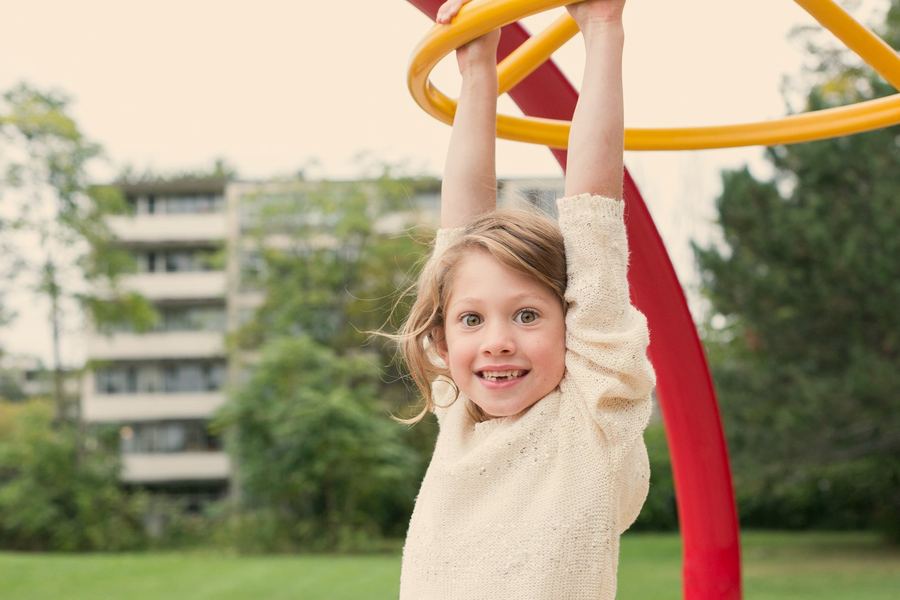 A grinning girl with a gap in her teeth hanging from playground rings