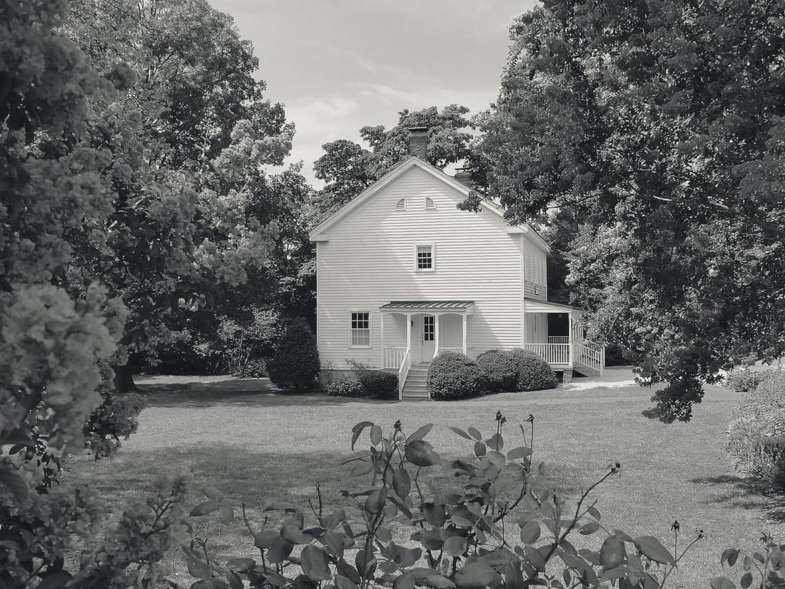 The white Freeman House store and museum behind crepe myrtles
