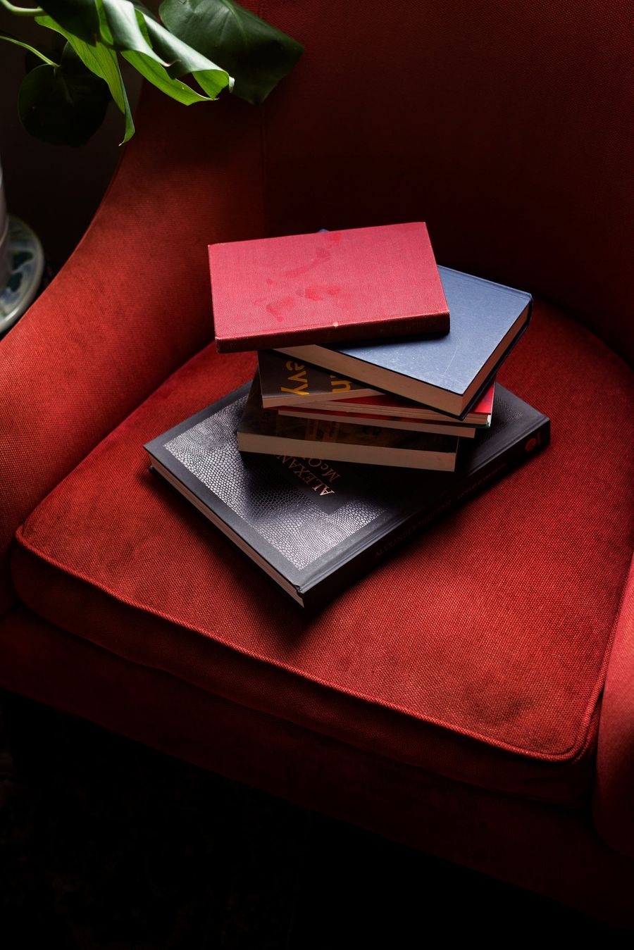 A stack of hardcover books resting on a red armchair