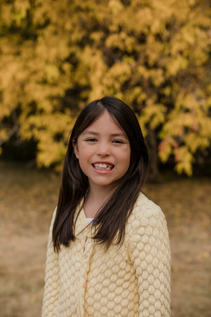 A smiling young girl in a knit cardigan in front of autumn leaves